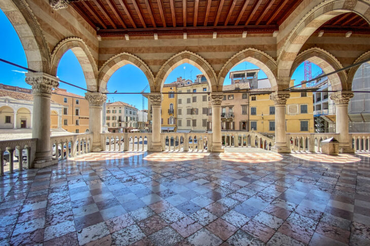 Loggia con arcate e pavimento a scacchi, affacciata su una piazza di Udine.