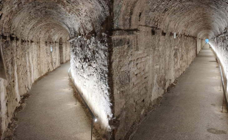 Una galleria sotterranea di contromina: lungo corridoio con volta in mattoni e pareti in pietra, illuminato lungo il camminamento.