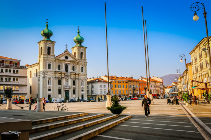 Piazza di Gorizia con la chiesa dalle due torri e gli edifici colorati.