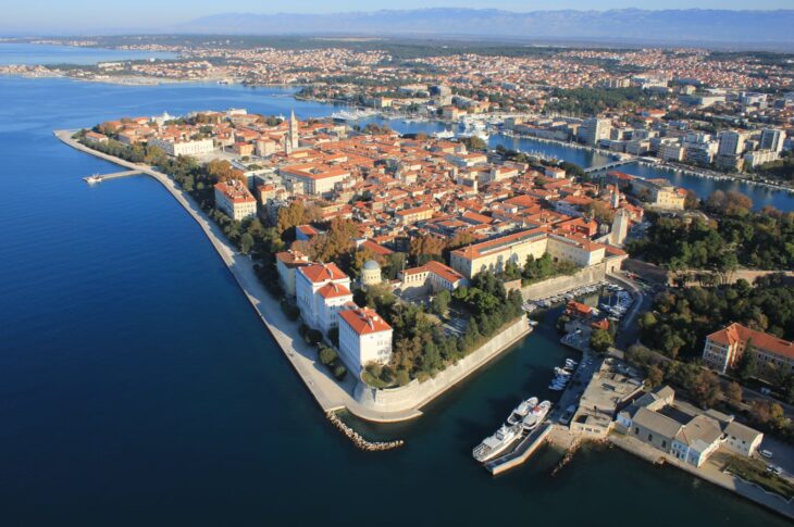 Vista aerea che ritrae la città storica di Zara (Zadar) situata sulla costa dalmata in Croazia. L'immagine mette in evidenza la penisola del centro storico, caratterizzata da edifici con tetti rossi e l'imponente campanile della cattedrale.